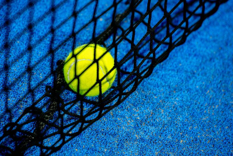 A padel ball resting against the base of the net