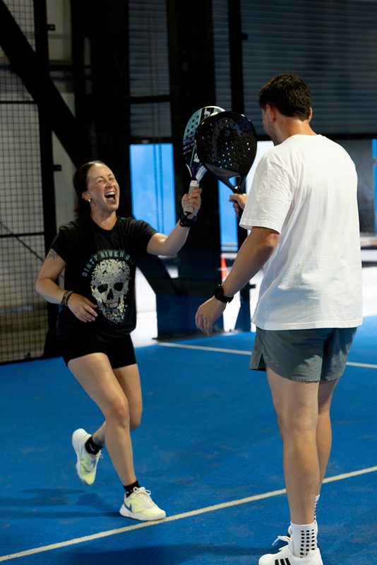 Two partners laugh and raise their paddles after winning a point at Foundry Padel