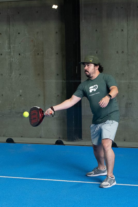A player meets a forehand in front of the bare concrete wall at Foundry Padel
