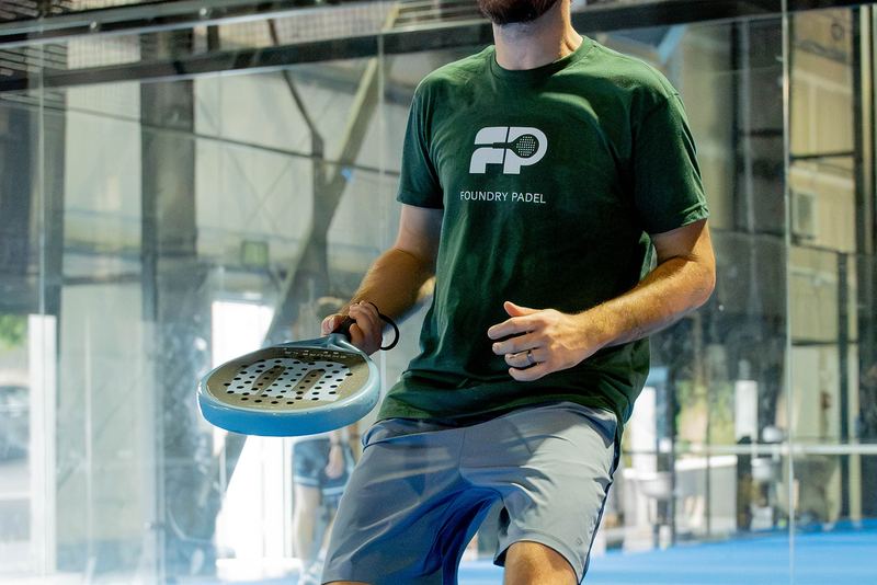 A member in a Foundry Padel tee spins a paddle between games