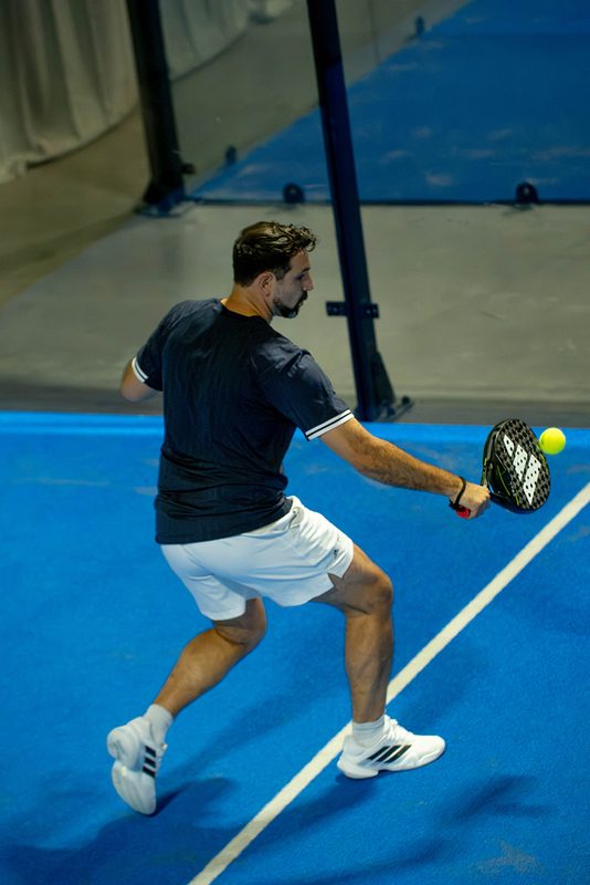 A player plays a low backhand right on the service line at Foundry Padel