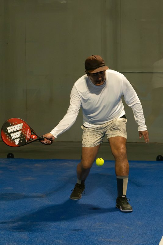 A player digs out a low backhand near the floor at Foundry Padel