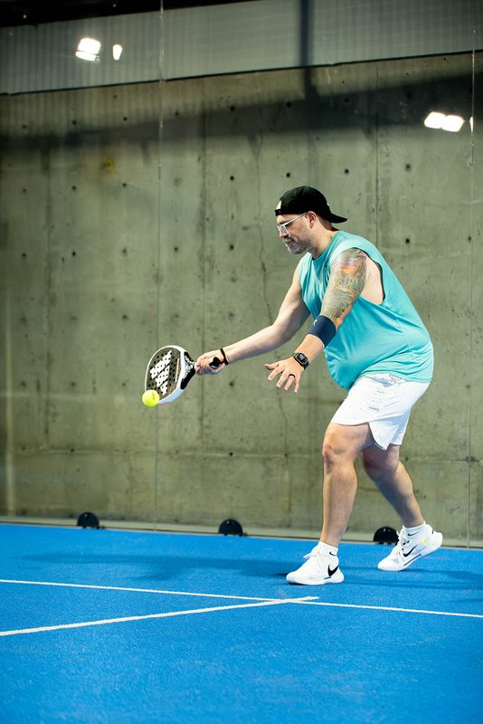 A player bends low for a forehand against the concrete back wall at Foundry Padel