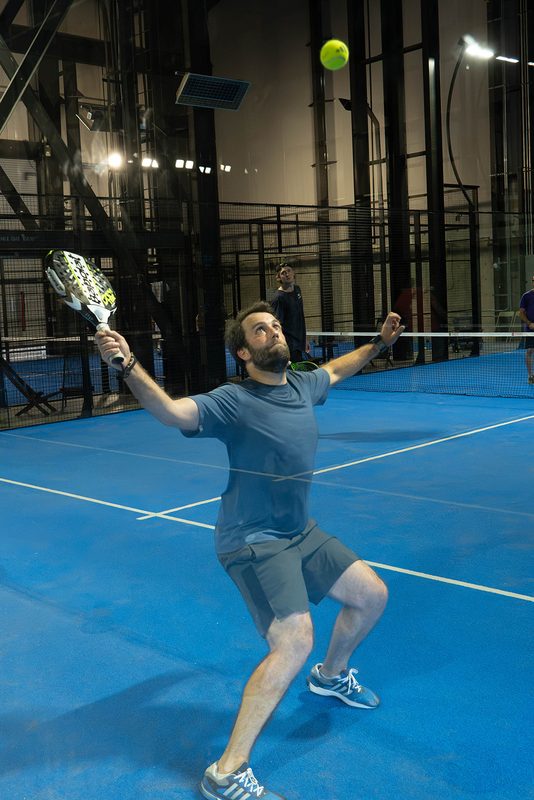 A player lunges under a high ball to play an overhead at Foundry Padel