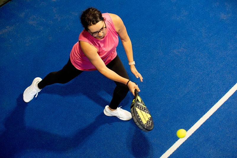 A player lunges for a low backhand, seen from above