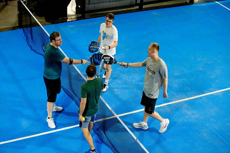 Four players meet at the net to tap paddles after a match at Foundry Padel