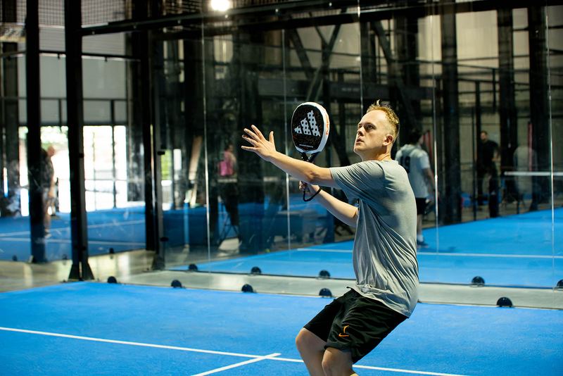 A player reaches for a high ball against the glass back wall
