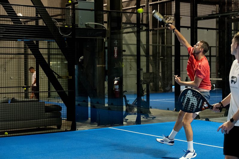 A player reaches full stretch for a smash under the court lights at Foundry Padel