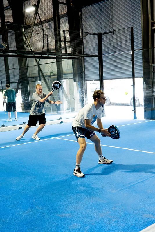 A player waits in the ready position with the rollup door open behind them at Foundry Padel