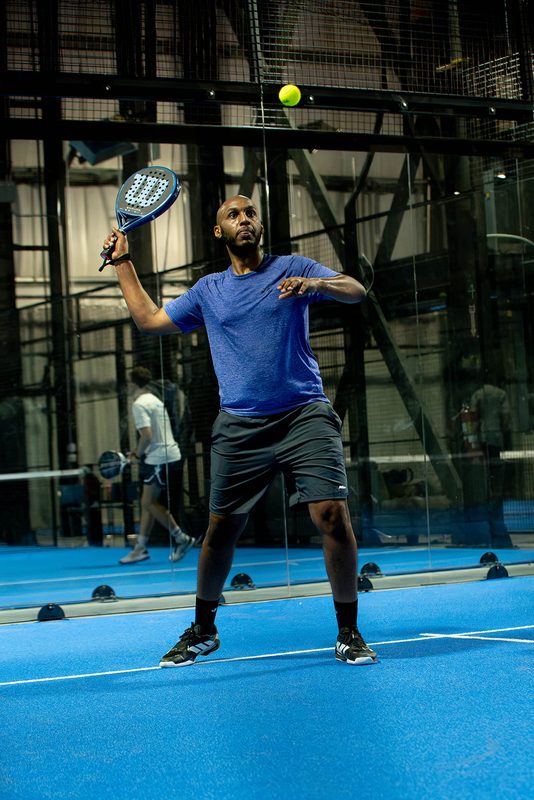 A player turns and lifts the paddle to meet a high ball at Foundry Padel