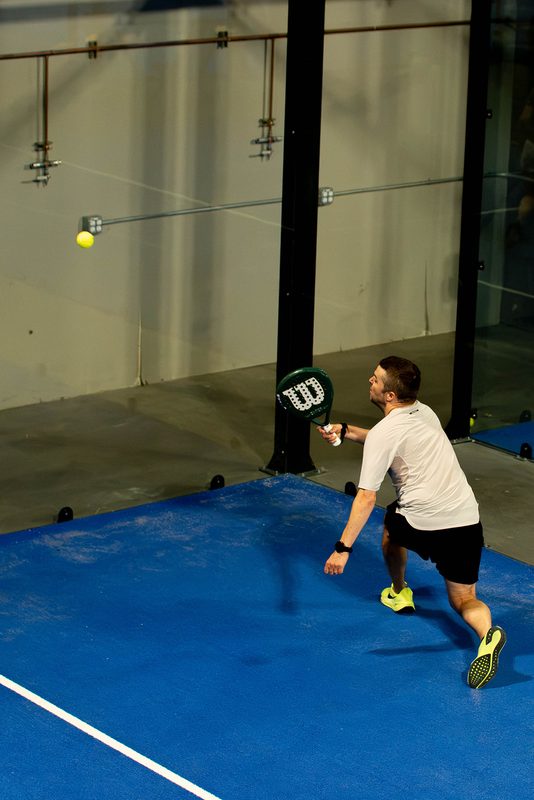 A player stretches wide for a volley under the warehouse roof at Foundry Padel