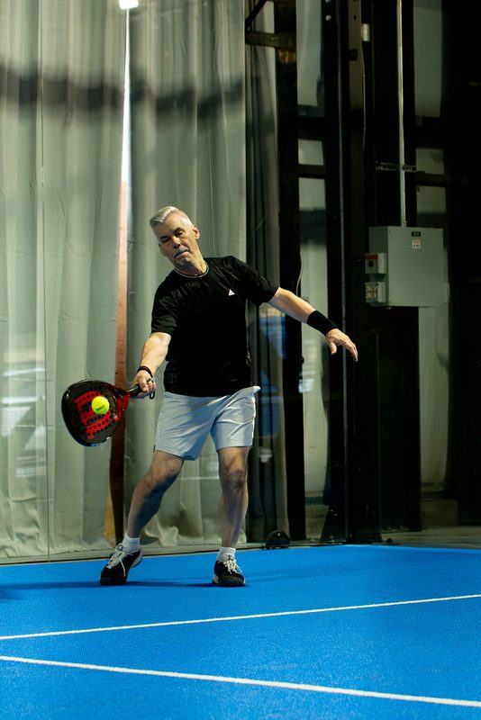 A player swings through a forehand in the back corner of the court at Foundry Padel
