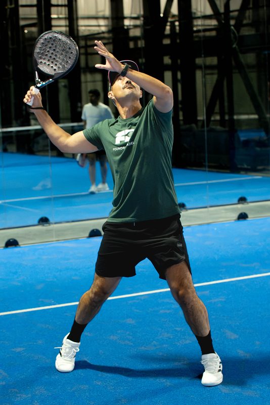 A player takes the paddle back behind the head to load up a smash at Foundry Padel
