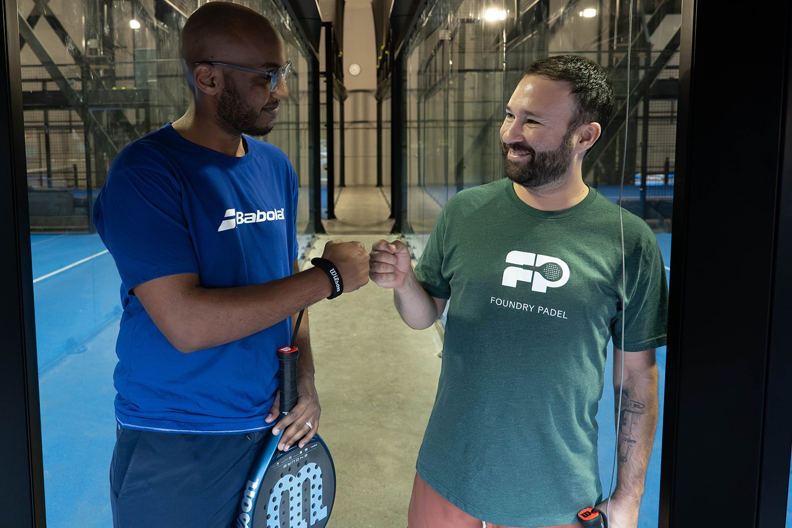Two members in Foundry Padel gear fist-bump between courts