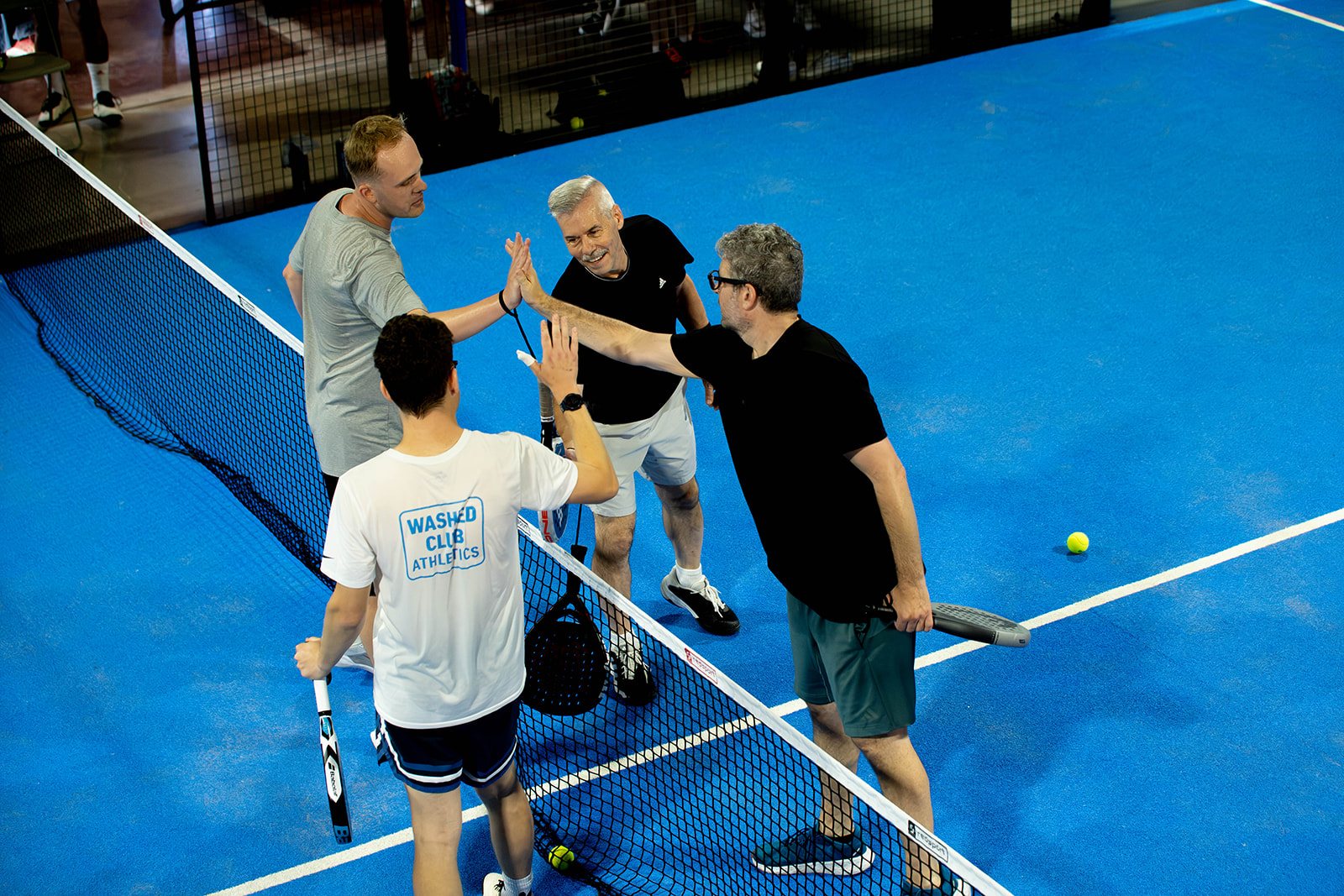 Four players high-five over the net at the end of a match at Foundry Padel