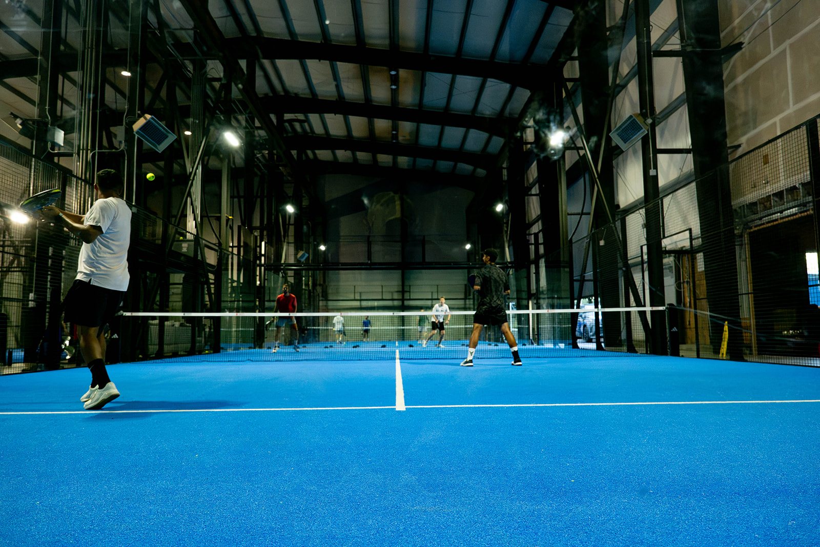 Amber light, exposed steel and concrete over the blue courts at Foundry Padel in St. Johns, Portland