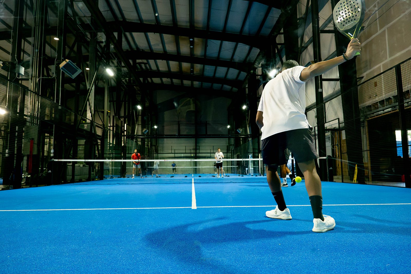 A player serves under the steel trusses of Foundry Padel's warehouse courts in Portland