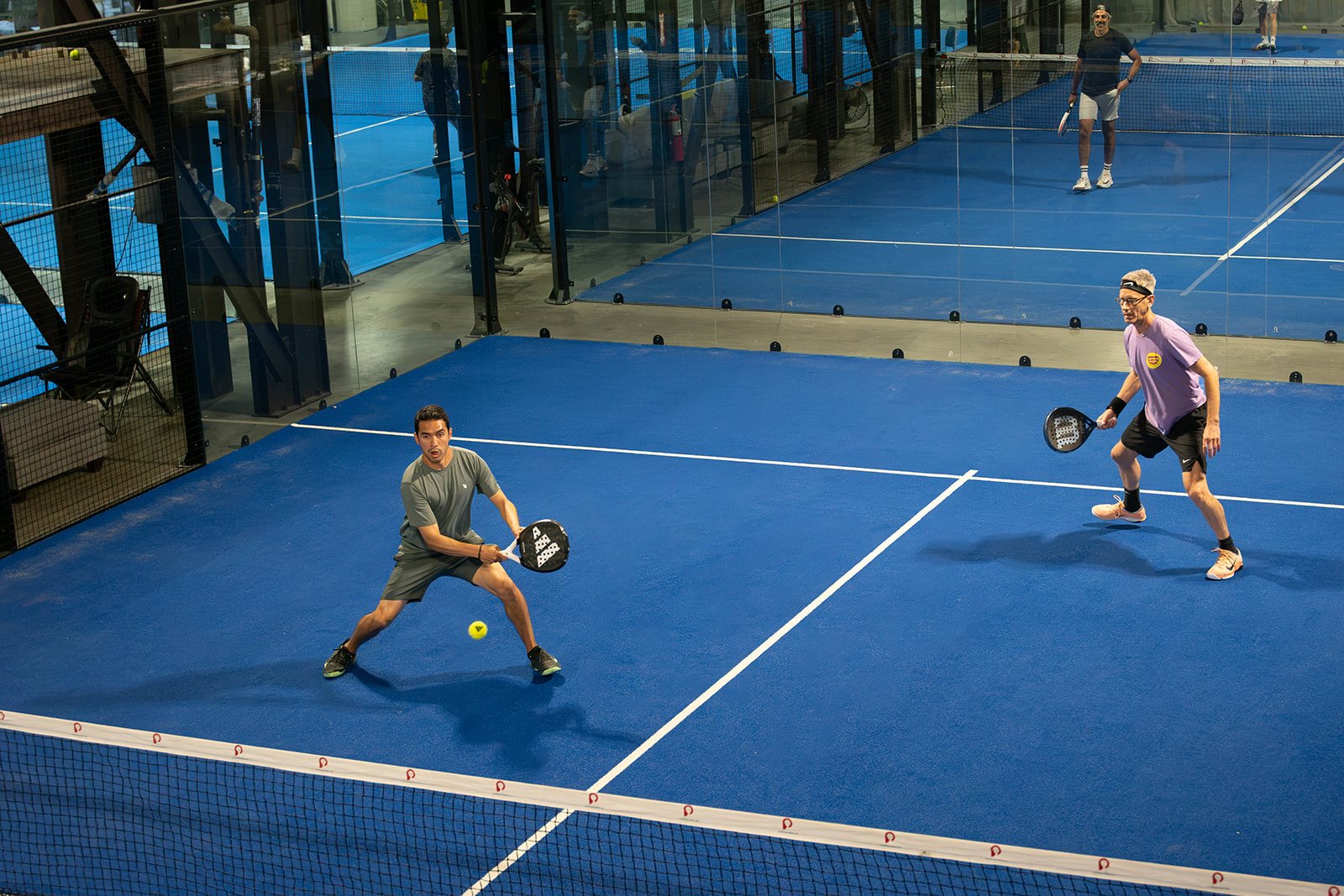 Two pairs rally across the net on a glass-walled doubles court at Foundry Padel