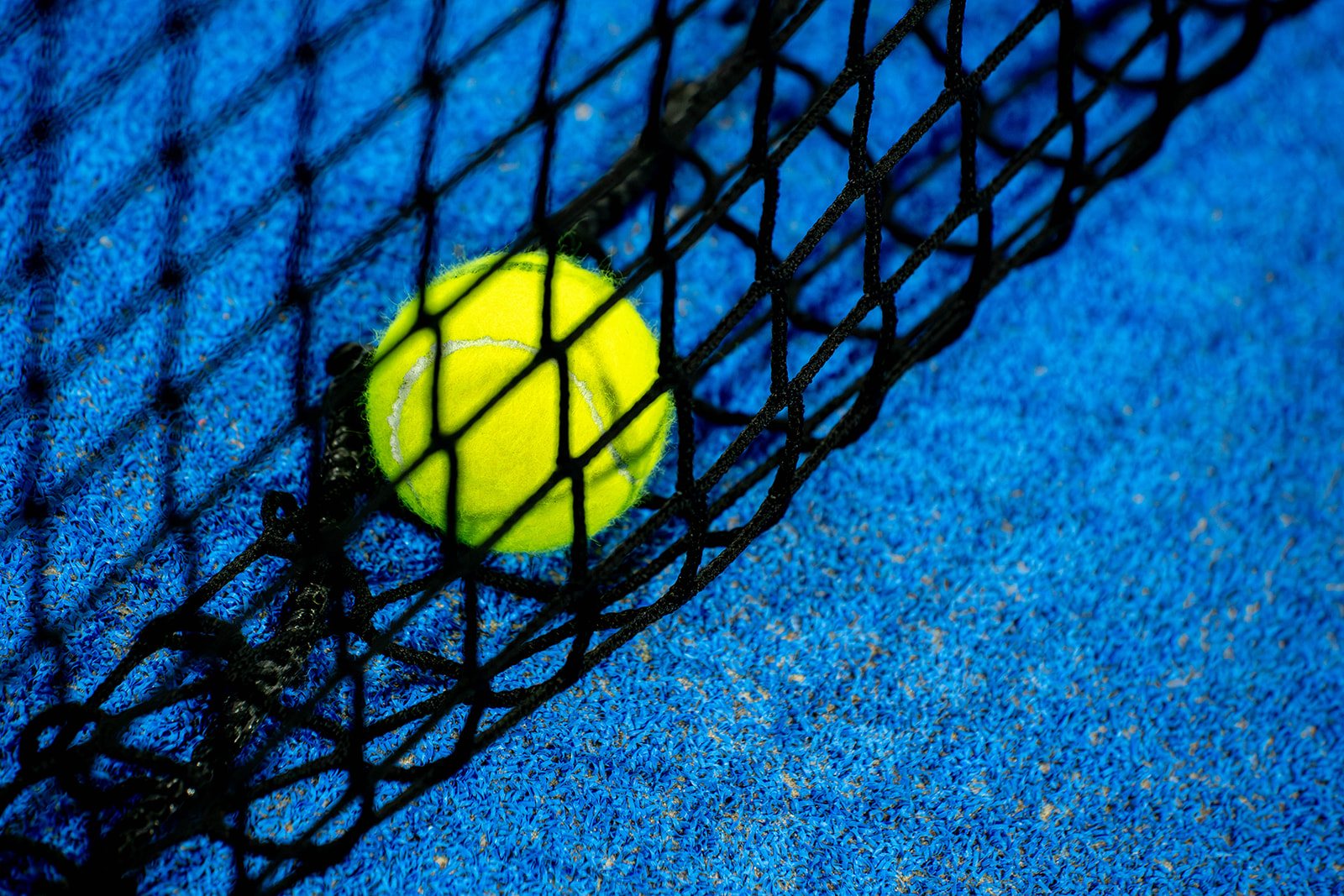 A padel ball resting against the net on Foundry Padel's blue court